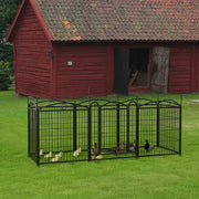 Black metal bird cage with birds in front of a red wooden building on grass.